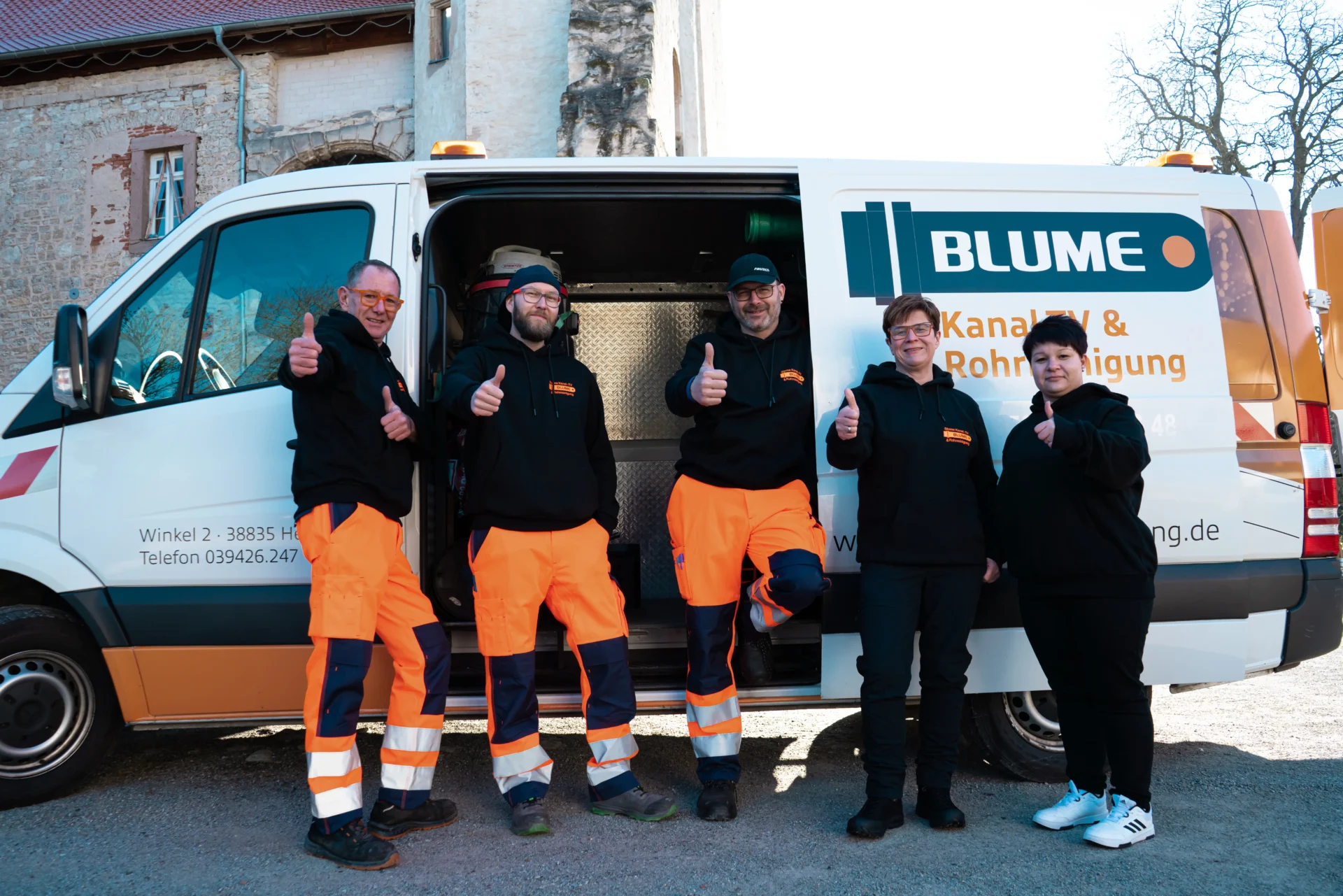 Team der Firma Blume Rohrreinigung in Arbeitskleidung steht vor einem Einsatzfahrzeug und lächelt in die Kamera.